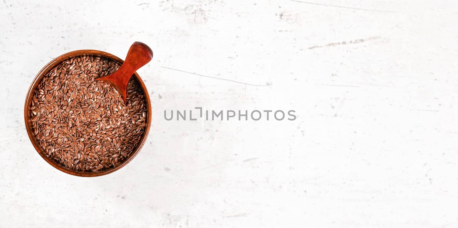 Common Flax linseed (Linum usitatissimum) seeds in small wooden bowl with scoop. View from above on white stone like board, space for text right side by Ivanko