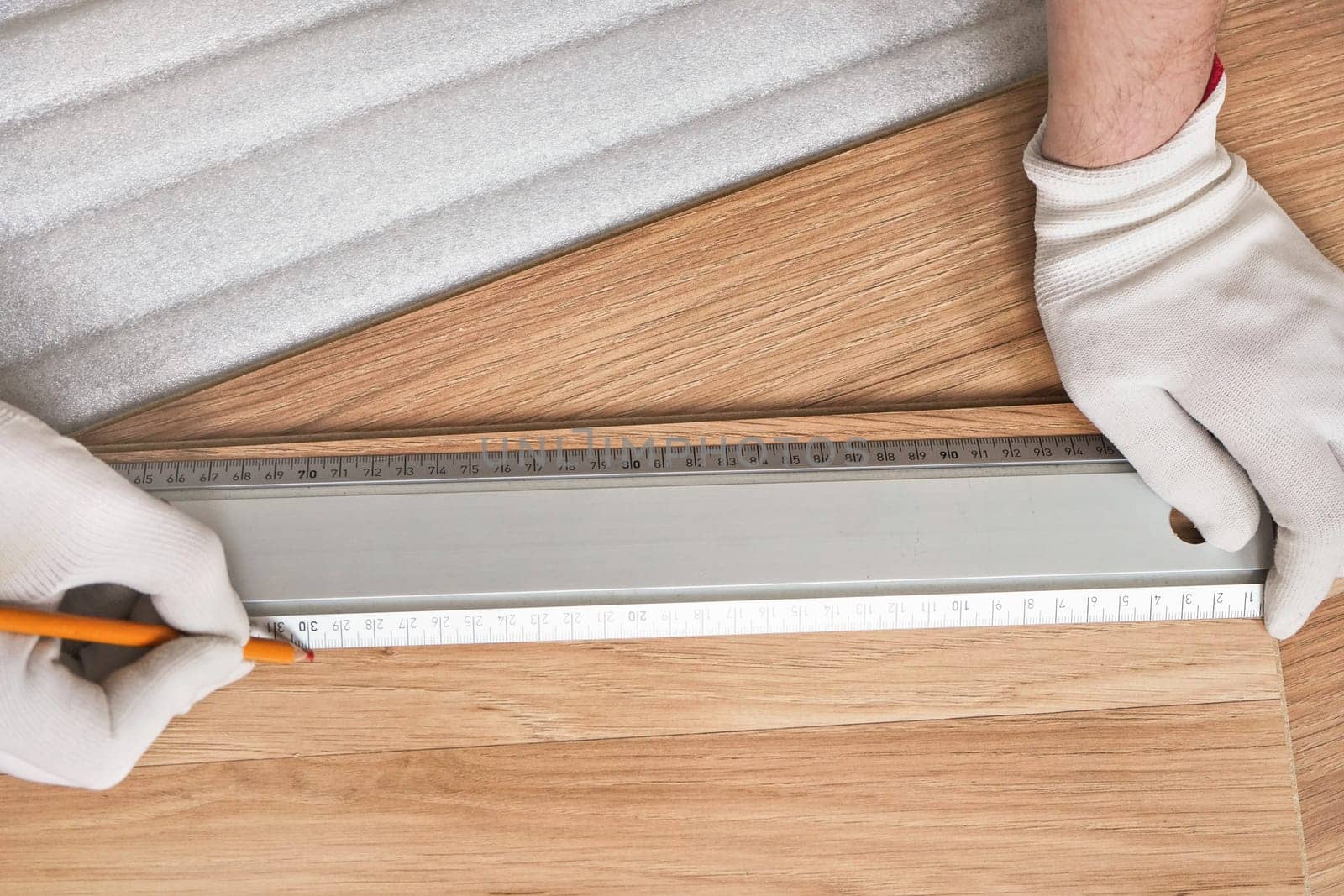 Installing laminated floor, detail on man hands in white gloves making mark with pencil using aluminium ruler