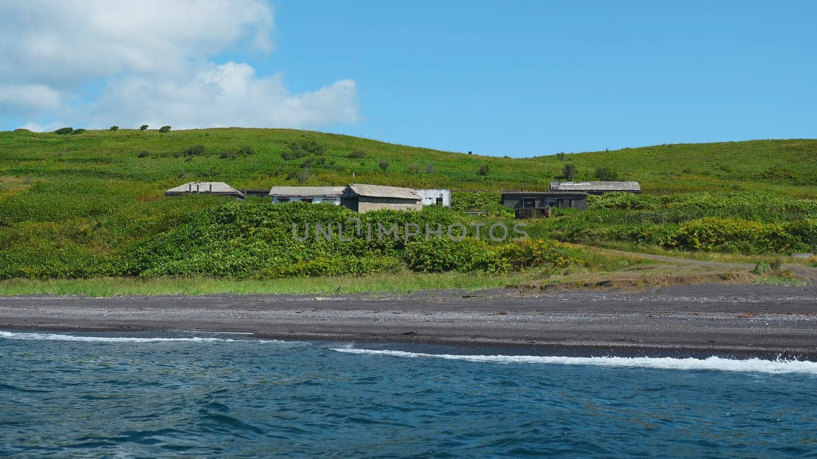 View from sea to shore with houses and greenery on sunny day. Clip. Swimming by shore with abandoned houses in dense greenery. Beautiful blue sea shore with remote houses on sunny summer day.