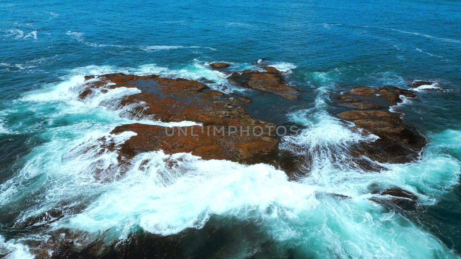 Aerial view of ocean waves crashing into rocks. Clip. Flying above turquoise water and giant boulders