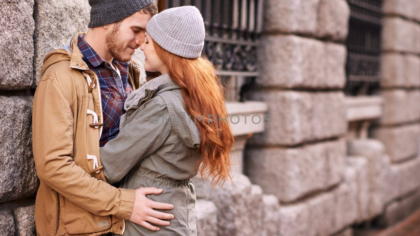 Couple, love and kiss with smile in outdoor or against wall in cold weather, together and support in London. Relationship, affection and bonding for romance with care, happiness and kindness.