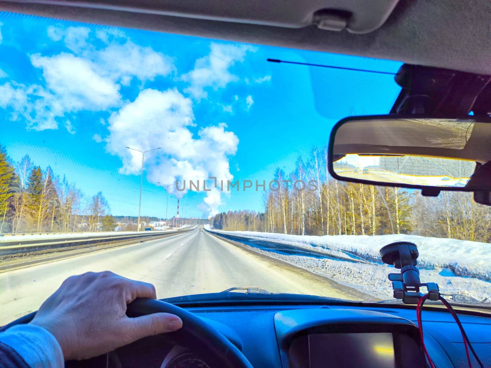 Winter Driving on a winter or spring Snow Lined Road Under sunny blue Sky. Drivers perspective on snowy road with sun And hand of woman on steering wheel
