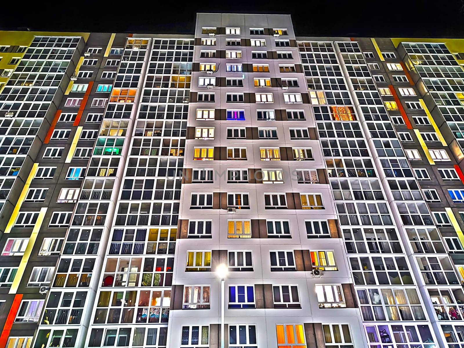 The facade of multi-storey building with multi-colored windows at night or in the evening. Background, texture, pattern