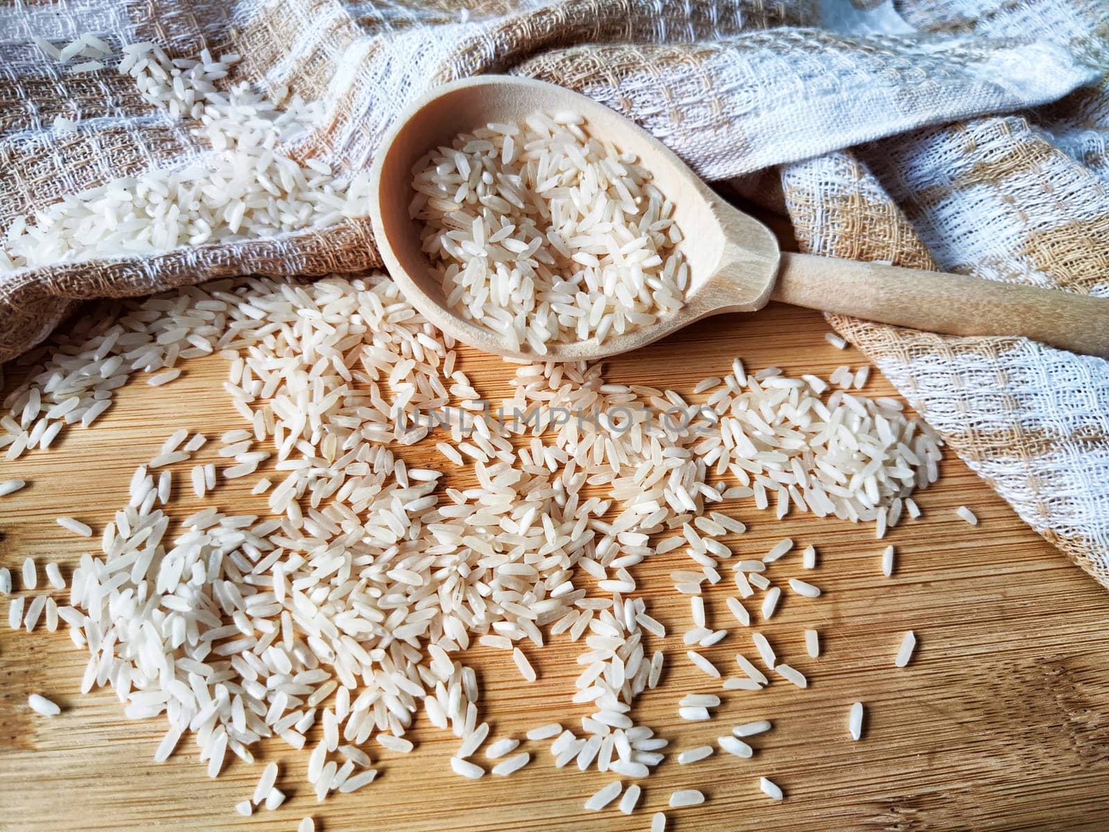 Rice scattered on textured fabric and in wooden spoon. Grits for cooking. Texture, background, copy space and place for text