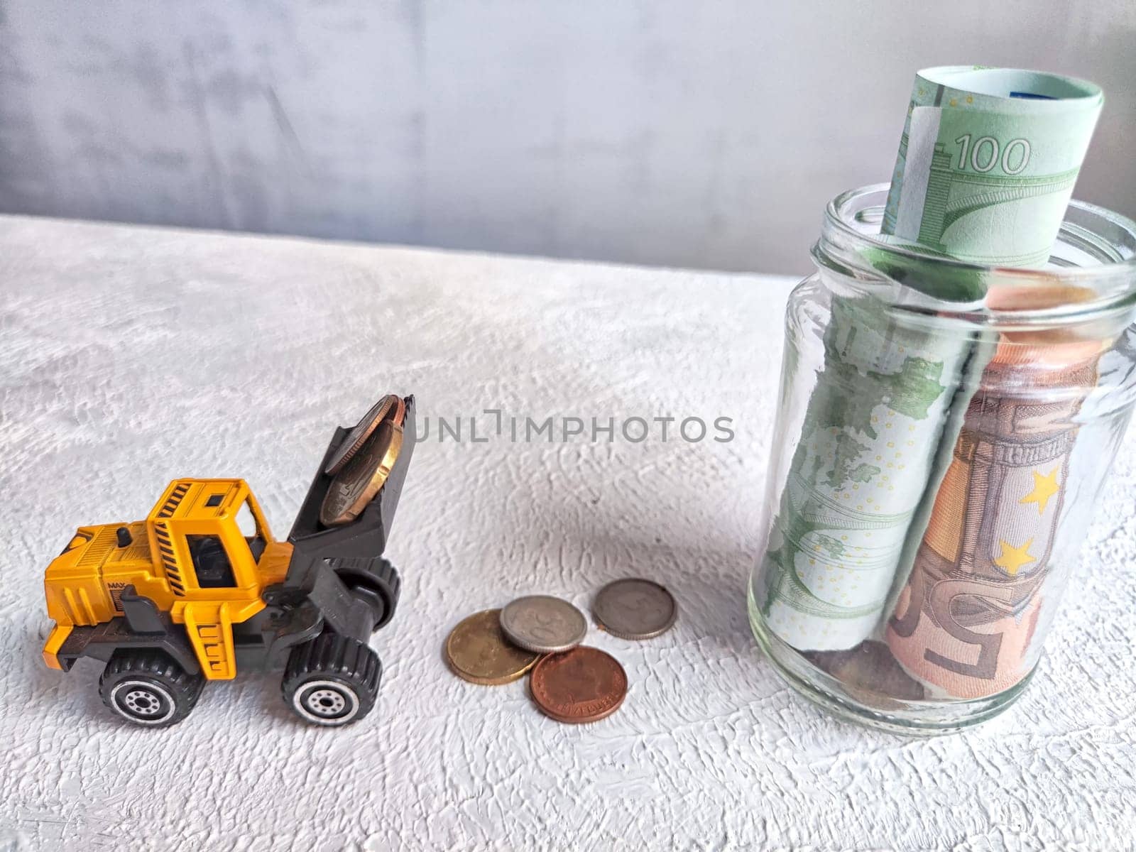 Toy Bulldozer Loading Coins Next to Jar of Cash. The concept of savings ranging from small money to large. The need for work to increase income