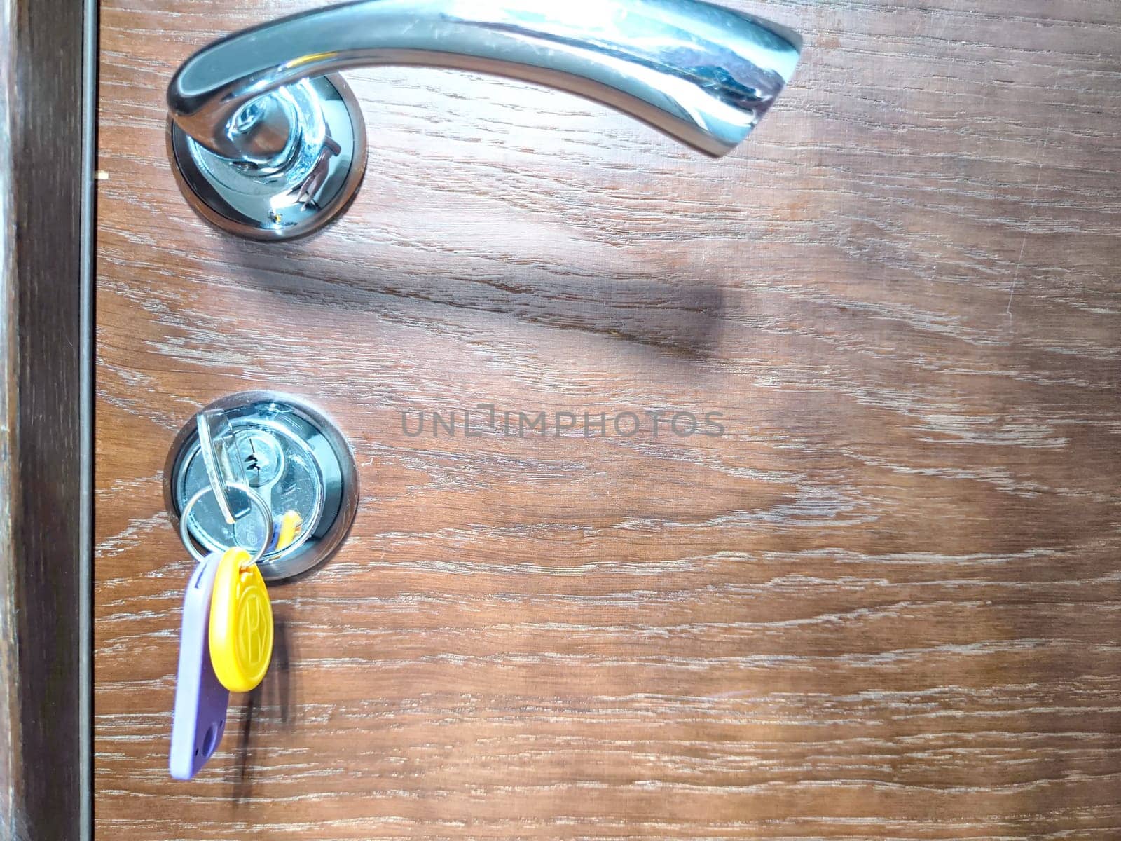Silver Door Handle and Keys in Lock at Residential or Hotel Entrance. Keys inserted into a door lock with handle above