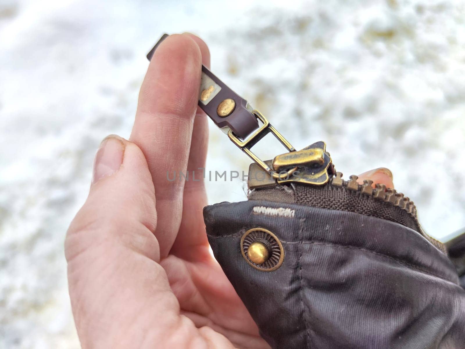 Fixing a broken zipper on a coat in woman hand outdoors during winter or spring
