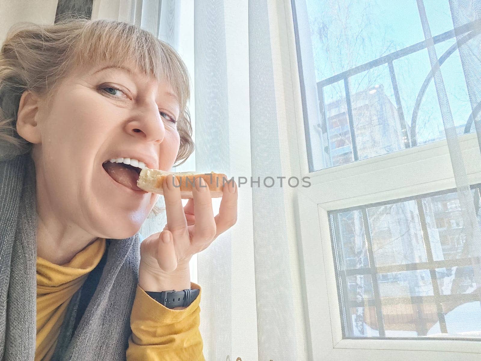 Mature Woman Enjoying Light Breakfast With Coffee by the Window. Woman in with morning coffee and bread. A blogger takes selfie while eating
