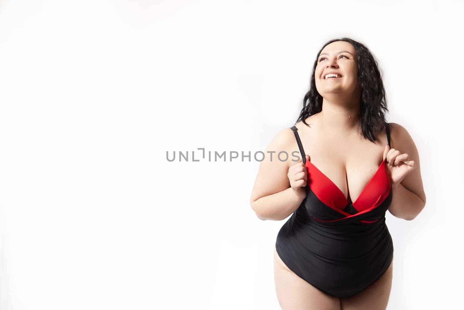 Portrait of attractive dreamy thick woman in red black swimsuit posing on white background. Body positive, photoshoot, selfie. Funny plus size model