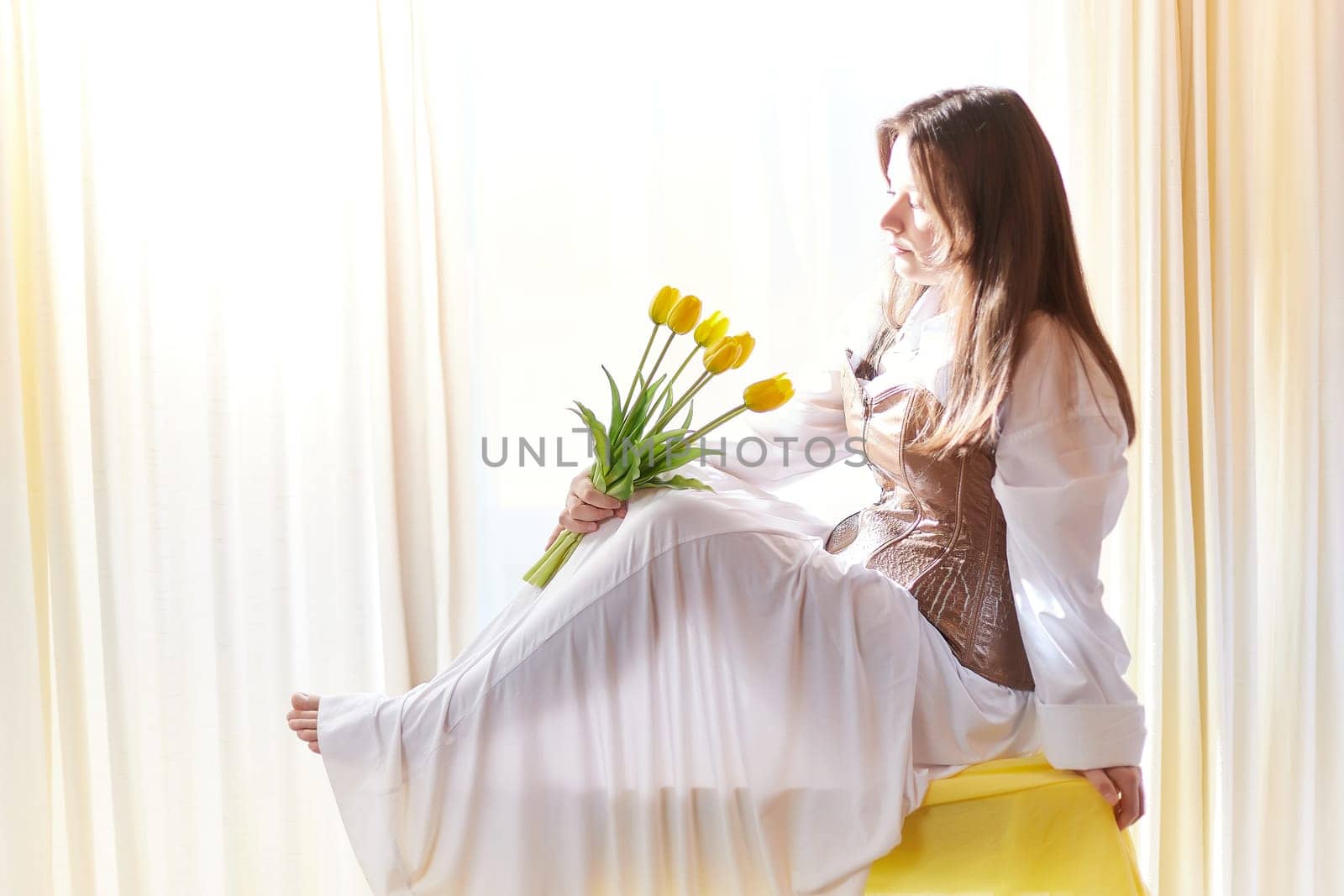 Beautiful sweet girl in nightgown in early morning with bouquet of delicate yellow tulips. Gift on International Women's Day on March 8th. Cosmetics, skin and hair care. Perfume, natural fragrance