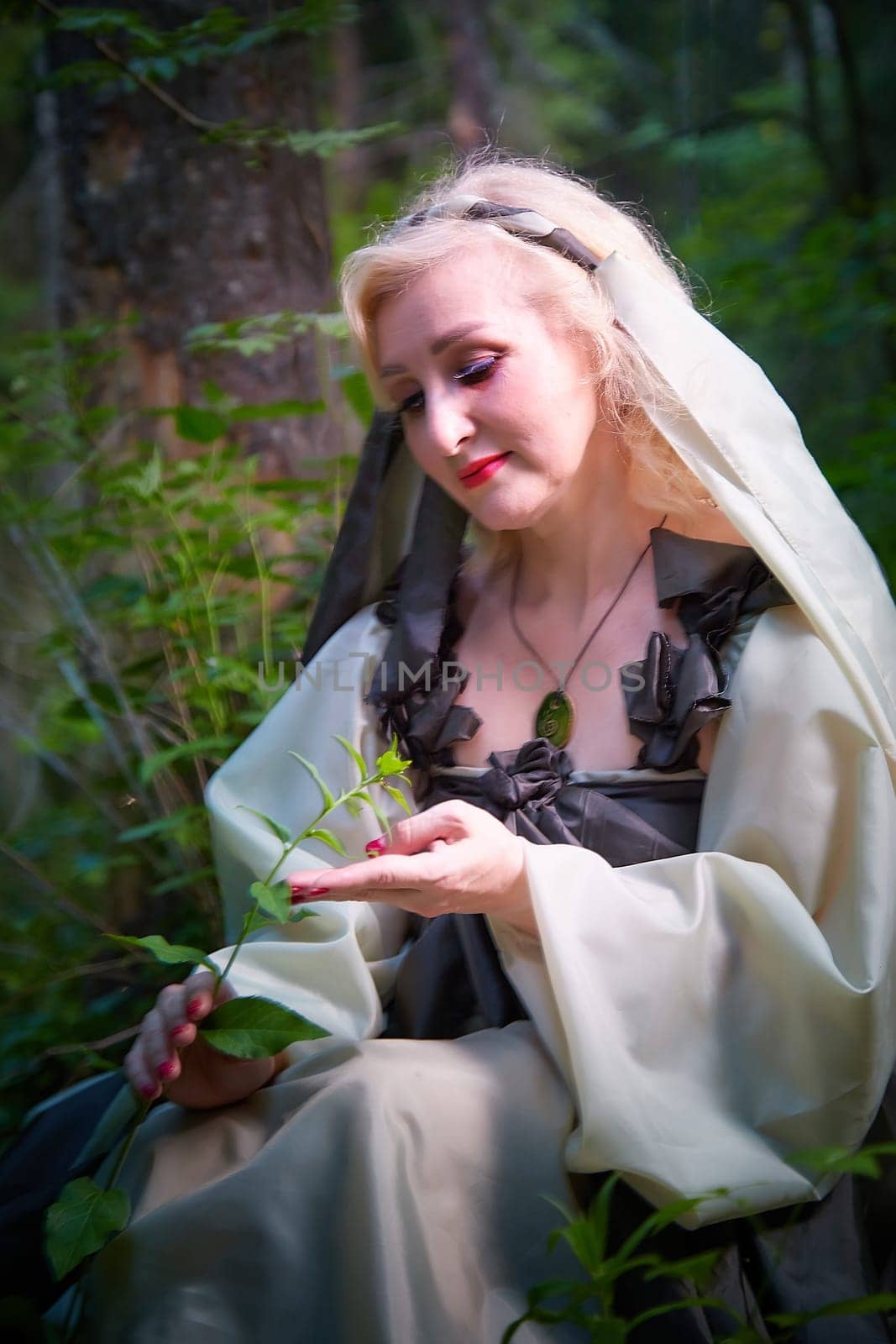 Adult mature woman 40-60 in a green long fairy dress in forest. Photo shoot in style of dryad and queen of nature. Fairy who loves nature in beautiful green summer forest. Concept of caring for nature by keleny