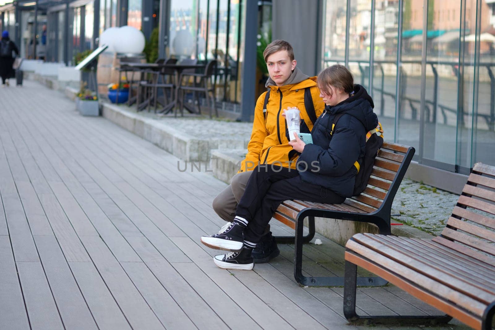 A teenage boy and girl relax on a bench by Ihar