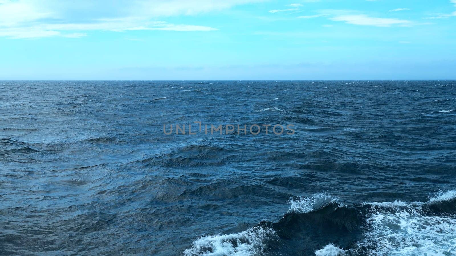 Beautiful view of horizon of blue sea with waves. Clip. Foam from waves in blue sea. In blue sea with waves on background horizon with blue sky.