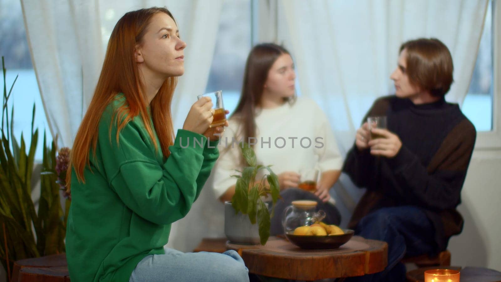 Side view of a happy relaxed woman enjoying tea and looking dreamy. Media. Blurred couple communicating on the background. by Mediawhalestock