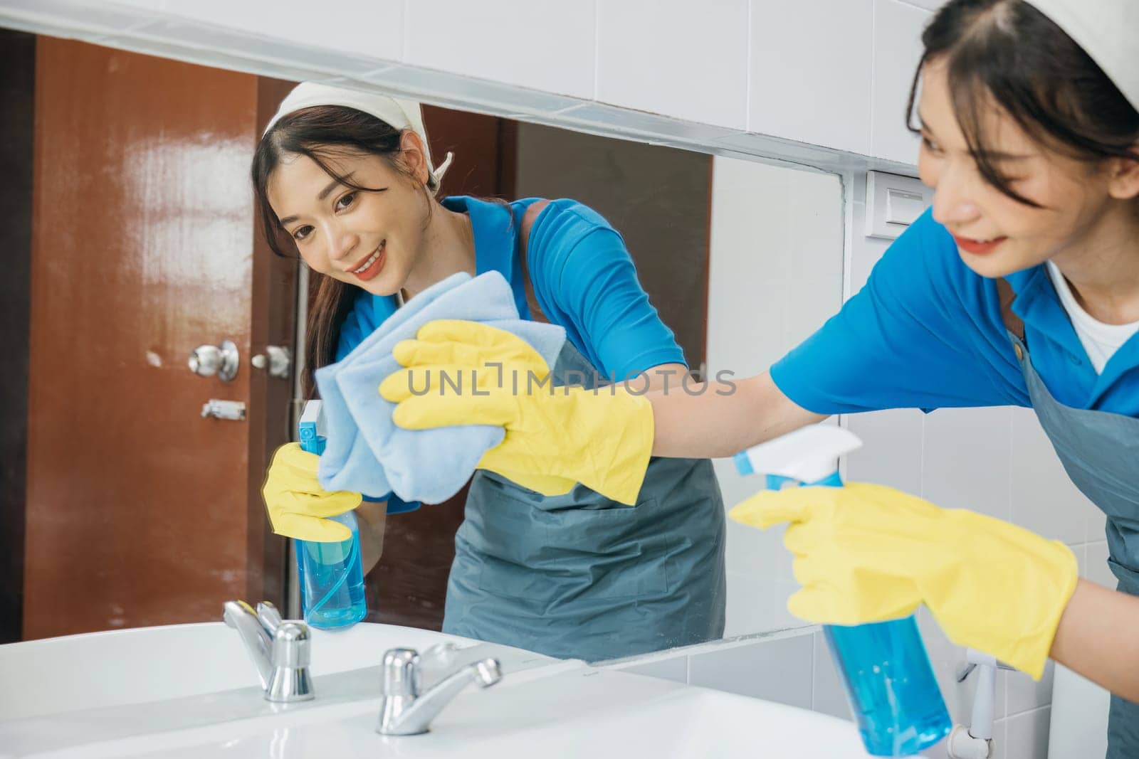 Maid with rubber gloves wipes bathroom mirror ensuring shiny reflection with a rag. Hotel service highlights professional cleaning ensuring purity and hygiene in modern settings. Maid cleaning at home by Sorapop
