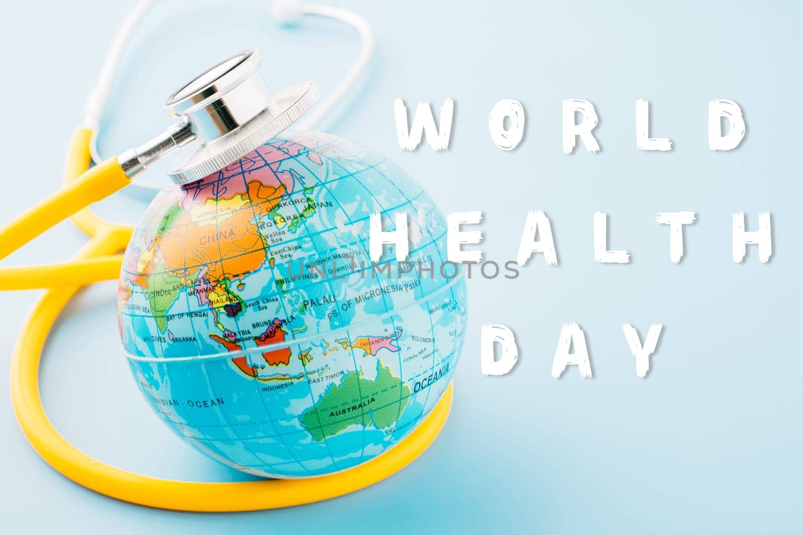 World Health Day. Top view yellow doctor stethoscope wrapped around world globe isolated on pastel blue background with copy space for text, Save world day, Health care and medical concept