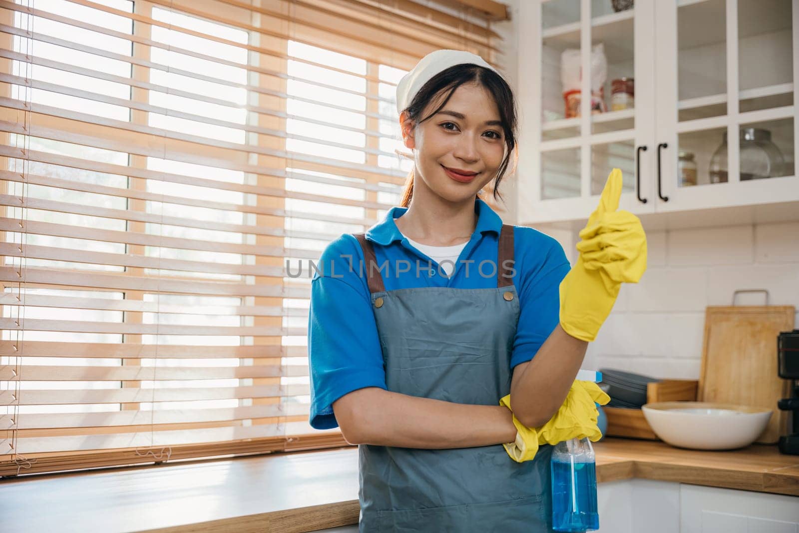 Young woman in apron and rubber glove prepared for home cleaning. Emphasizing housekeeping and hygiene with spray bottle. Clean disinfect home care. maid with liquid. by Sorapop