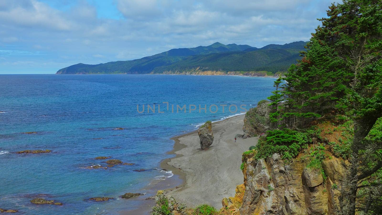 Beautiful view of bend of coast with rocks on sunny day. Clip. Landscape of rocky coast with green mountains and forest. Beautiful beach with rocks and blue sea on sunny day by Mediawhalestock