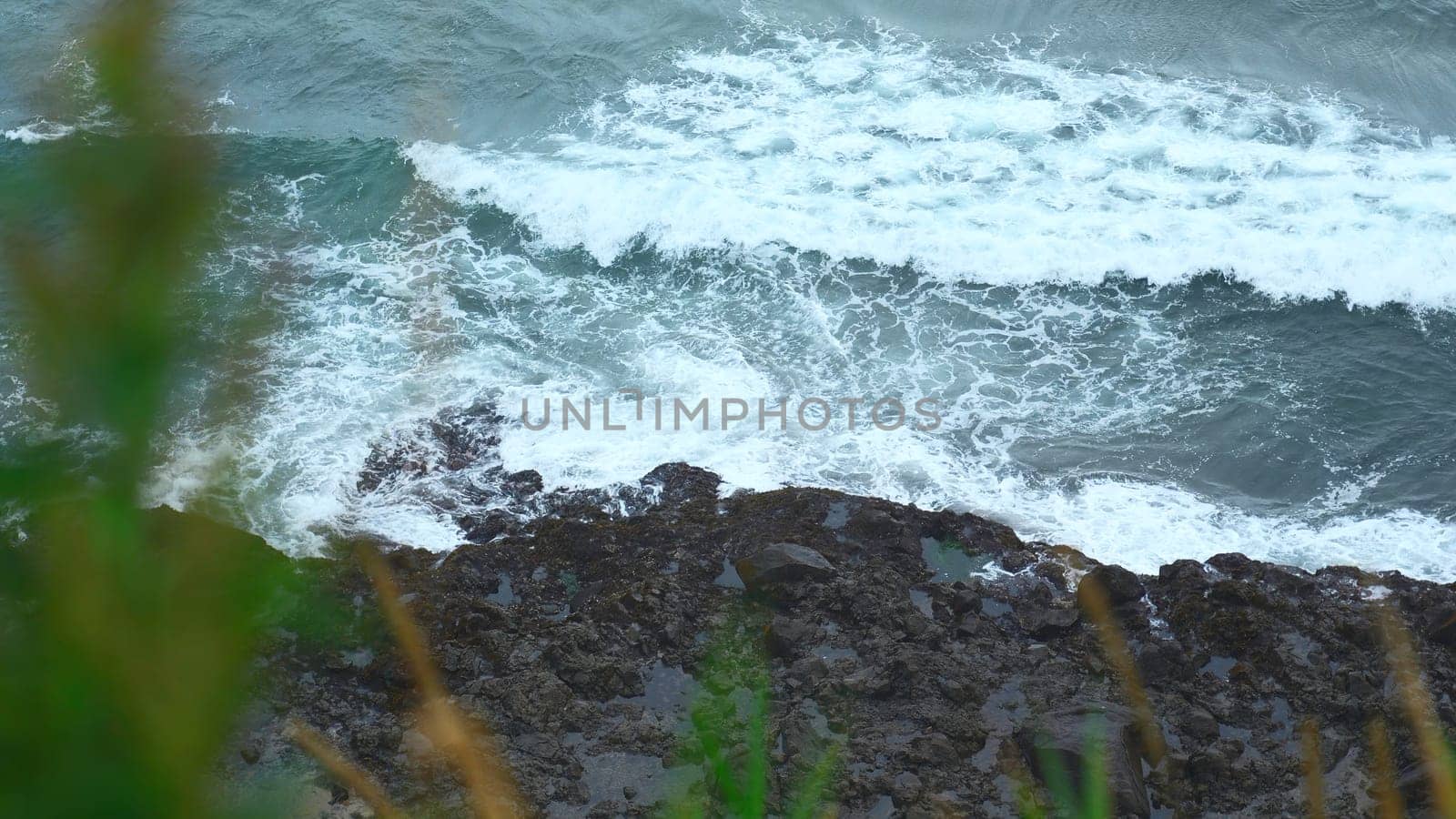 Close-up of surge of waves on rocky shore. Clip. Beautiful waves with splash roll on stones of seashore. Beautiful splashes of waves crashing on rocks on cloudy day.