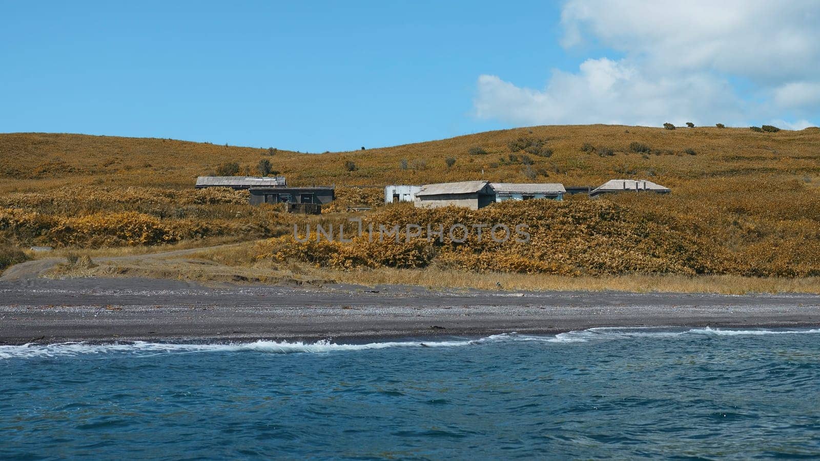 View from sea to shore with houses and greenery on sunny day. Clip. Swimming by shore with abandoned houses in dense greenery. Beautiful blue sea shore with remote houses on sunny summer day.