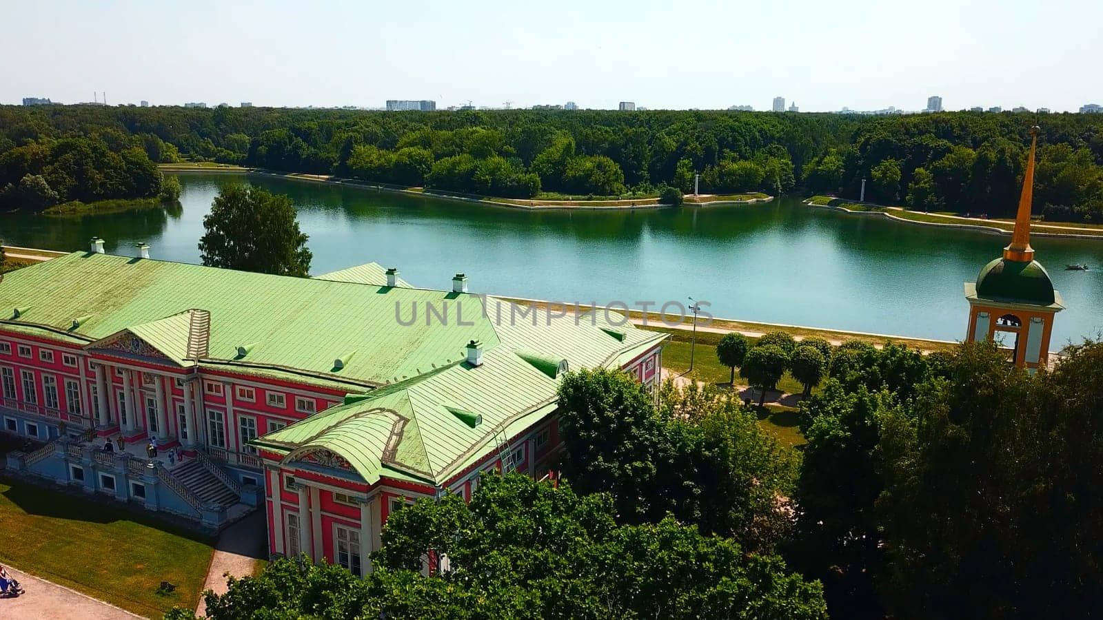 Top view of historic building by river with forest. Creative. Beautiful historical suburb with tourists on riverbank. Picturesque estate on river bank with forest on sunny summer day.