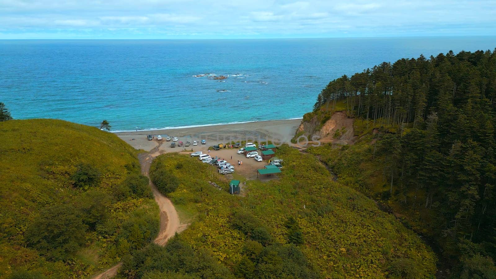 Top view of green forest on coast with tourists and turquoise water. Clip. Amazing landscape with green forest on coast with turquoise sea. Tourists relax on shore of mountain coast of ocean.