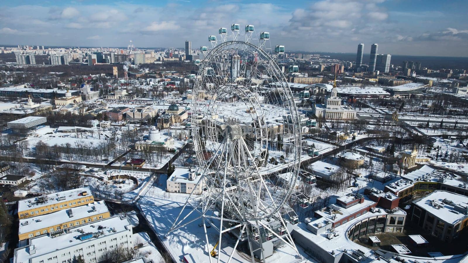 Top view of big Ferris wheel in winter. Creative. Beautiful urban landscape with Ferris wheel in city center in winter. Ferris wheel in center of big city on sunny winter day by Mediawhalestock