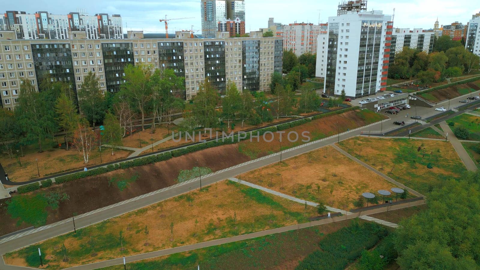 Top view of park alley in residential area of city. Clip. View of city with residential buildings and park alley. Beautiful landscape of park alley in urban landscape with buildings.