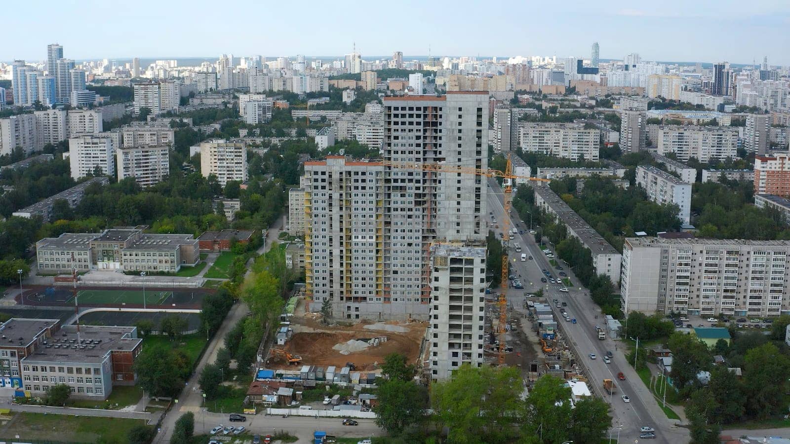 Top view of city with construction of high-rise building. Stock footage. Construction of multi-storey complex in residential area of modern city. Construction of high-rise building with crane on background of panorama of city by Mediawhalestock