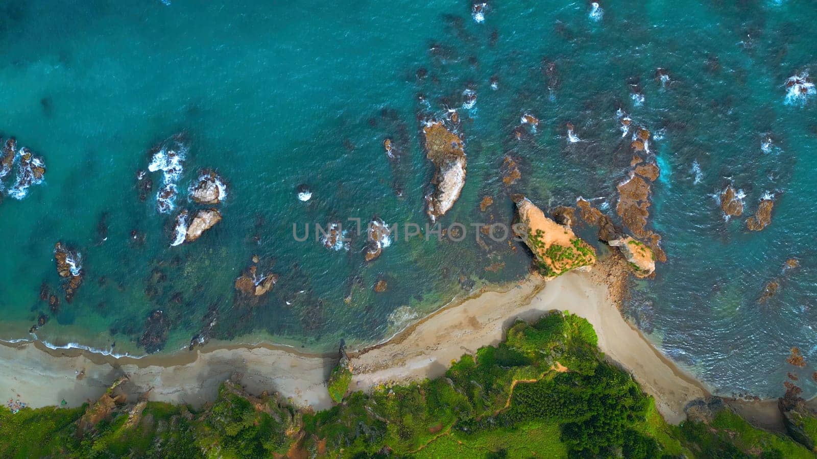 Top view of coast with rocks in water and forest. Clip. Amazing nature of coast with beautiful rocks and clear water. Wild coast with rocks in turquoise water and green forest on sunny day.