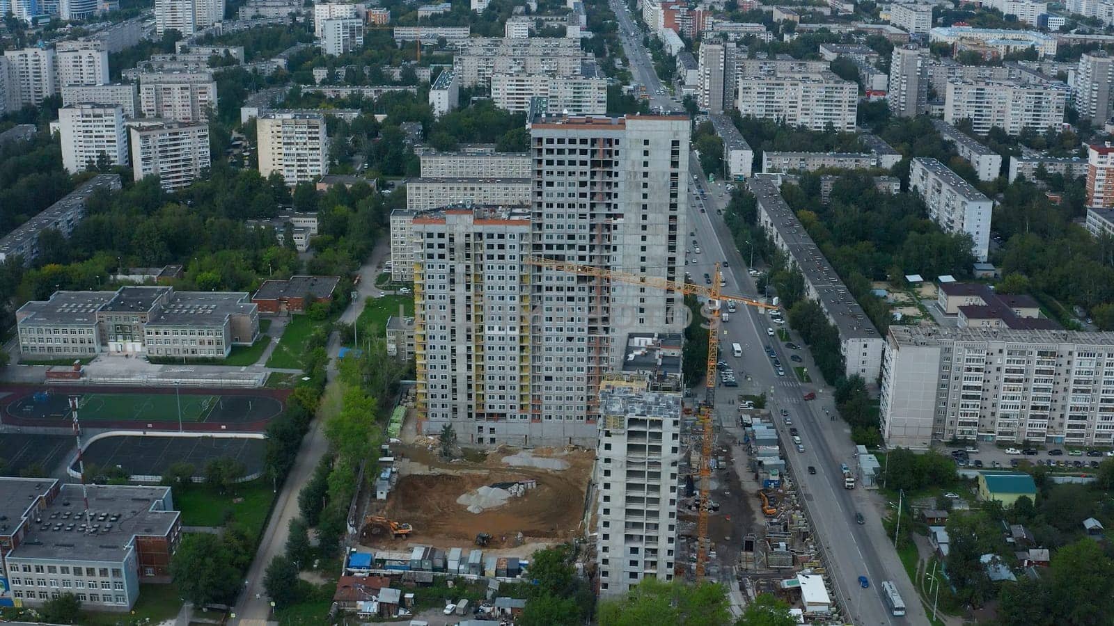Top view of city with construction of high-rise building. Stock footage. Construction of multi-storey complex in residential area of modern city. Construction of high-rise building with crane on background of panorama of city.