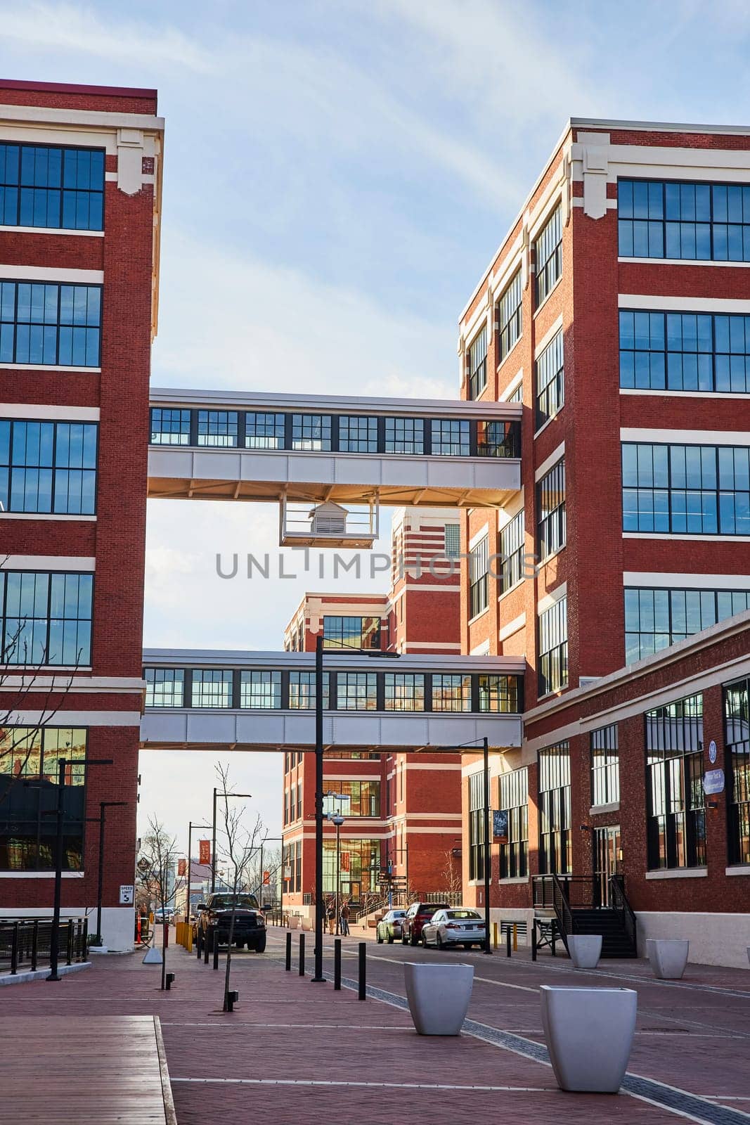 Modern urban renewal at Electric Works, Fort Wayne, Indiana shows vibrant red-brick buildings connected by a pedestrian bridge, symbolizing connectivity and innovation.