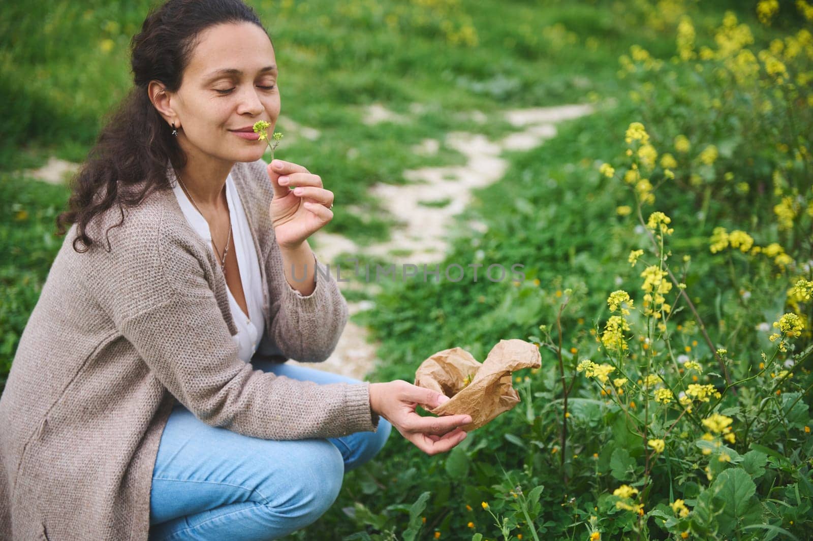 Happy smiling woman herbalist, botanist sniffing flower while picking medicinal herbs for aromatherapy or preparing herbal tea according to traditional recipe. Naturopathy. Herbal alternative medicine