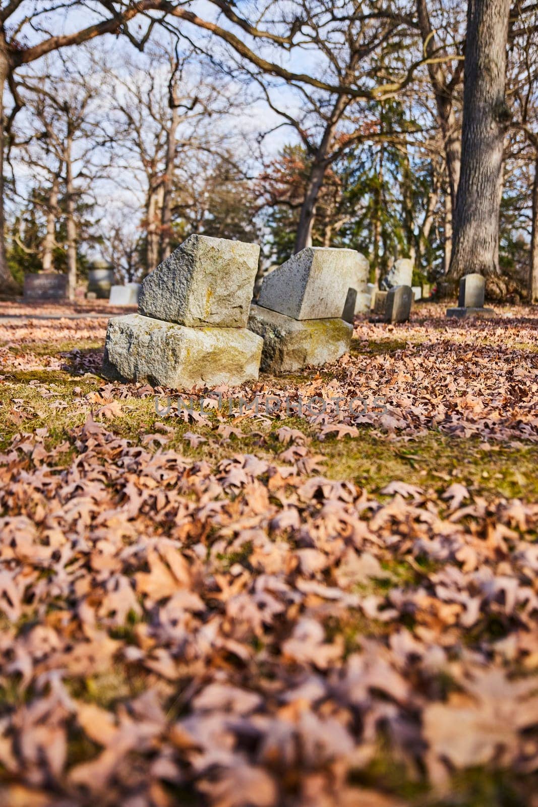 Fallen gravestones amidst autumn leaves in Lindenwood Cemetery, Indiana, capturing the serene melancholy of time's passage.