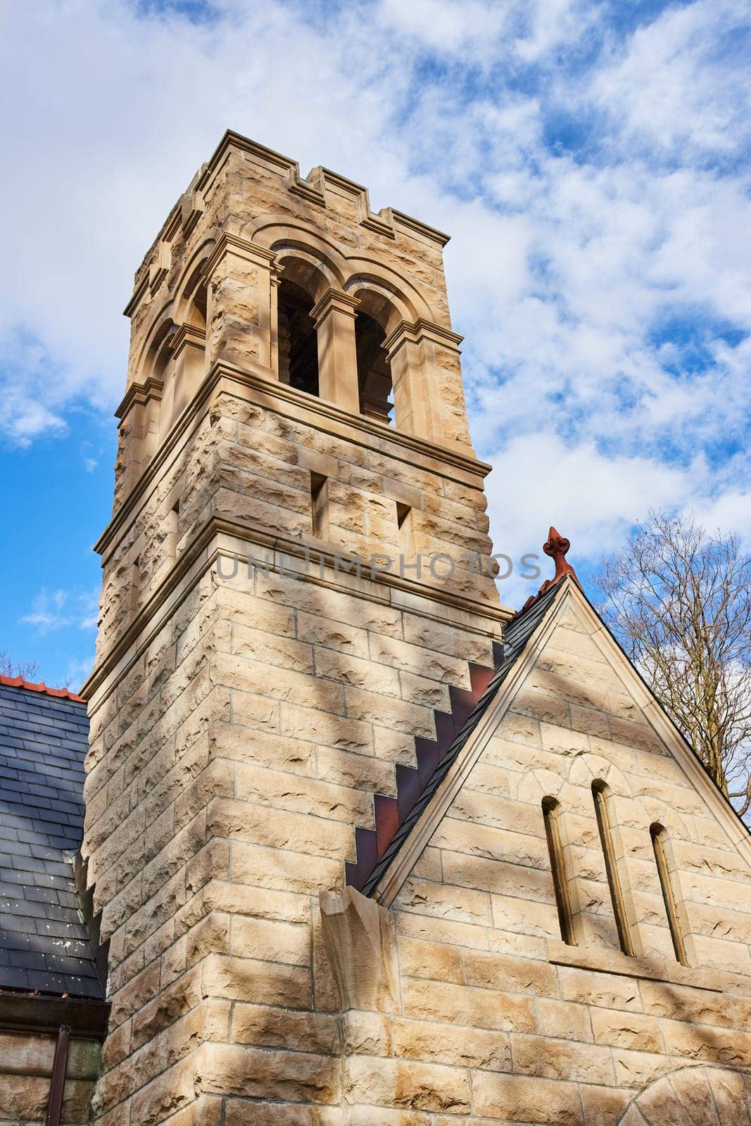 Imposing stone tower from historic church, displaying craftsmanship and durability, rising against a partly cloudy sky in Lindenwood Cemetery, Fort Wayne, Indiana.