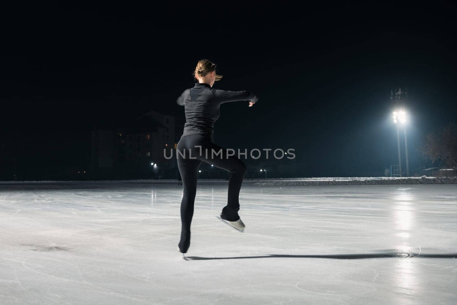 Beautiful young woman ice skating and performing she program over city outdoor ice arena. Winter activities concept