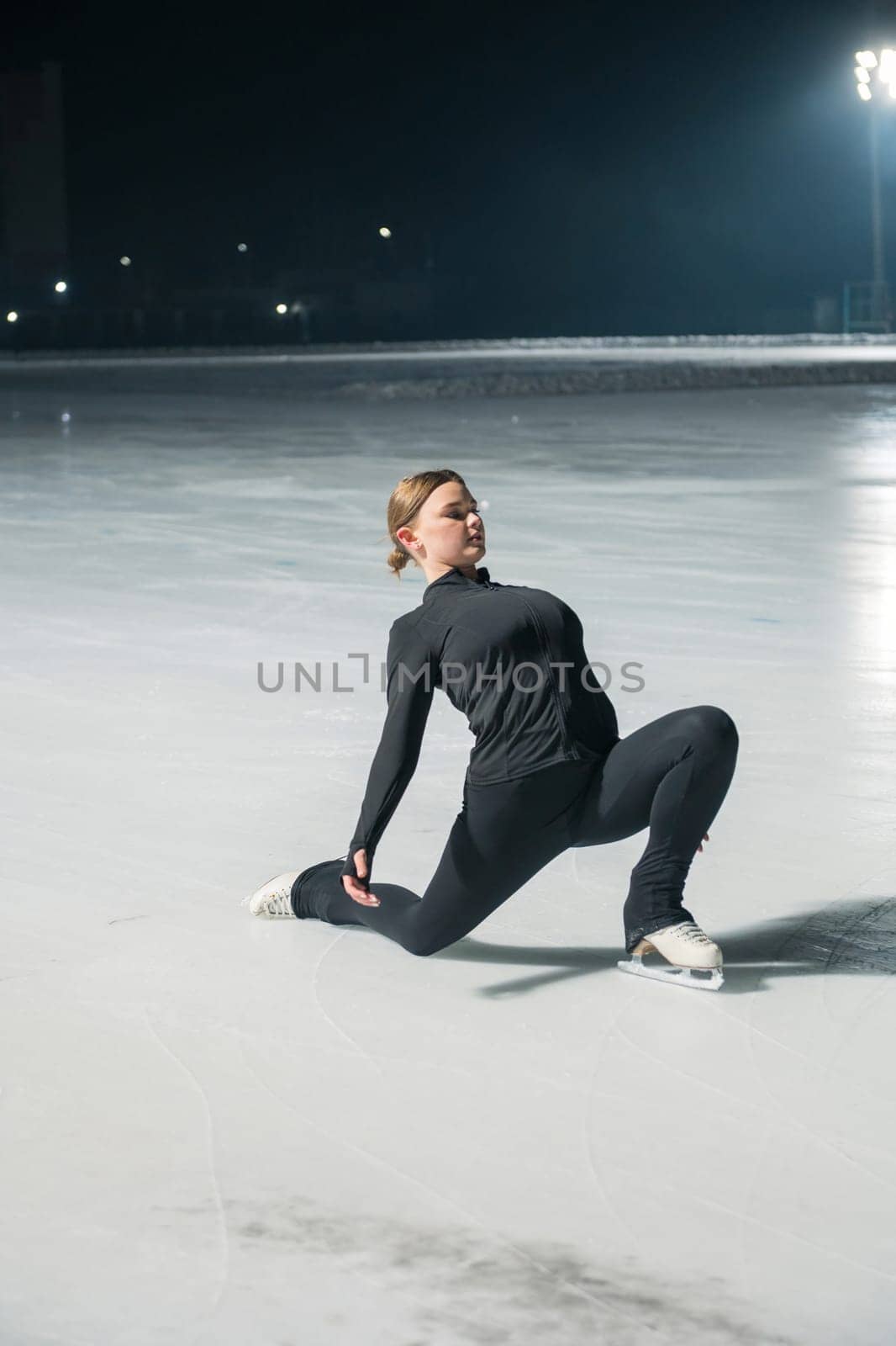 Beautiful young woman ice skating and performing she program over city outdoor ice arena. Winter activities concept