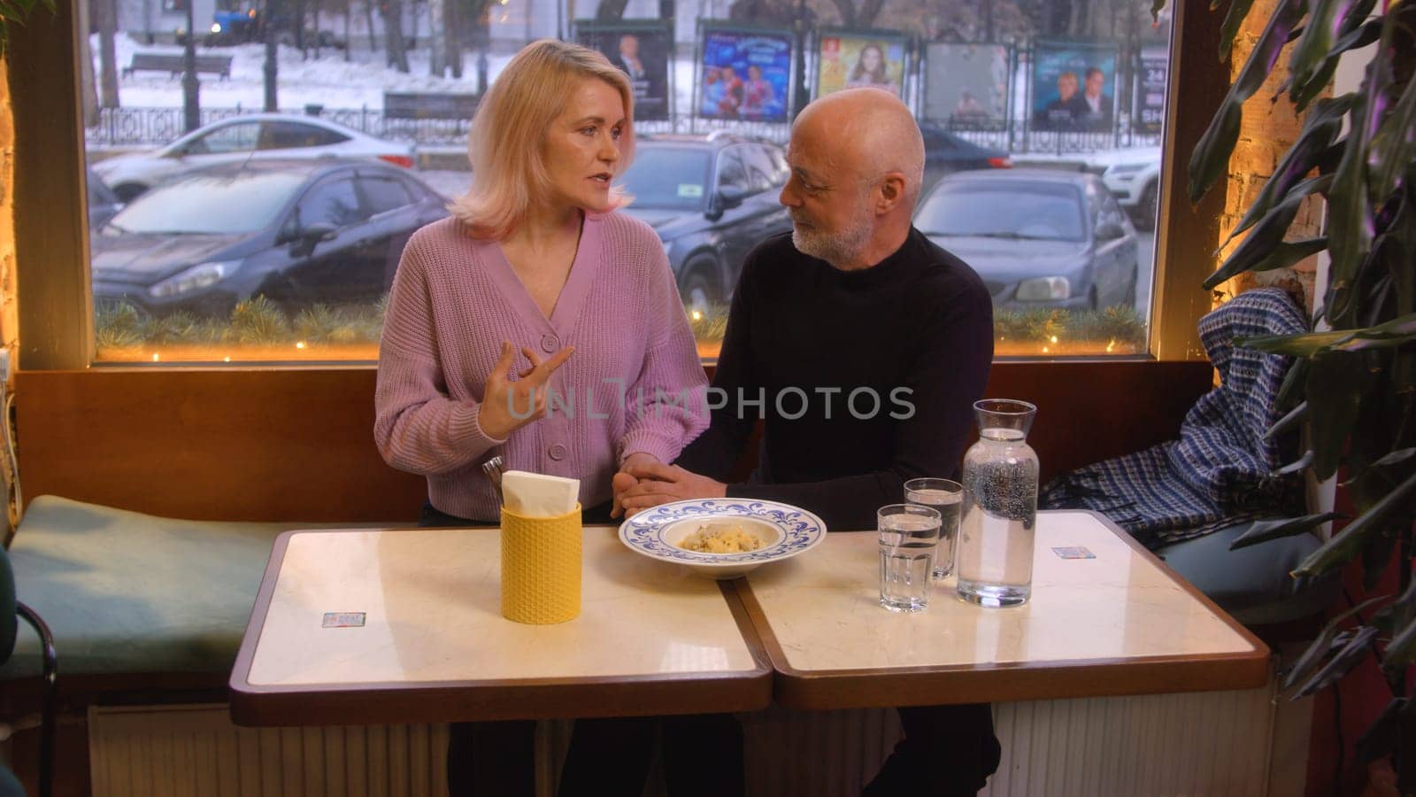 Beautiful elderly couple is chatting in cafe. Stock footage. Elderly couple is chatting sweetly on date in cafe. Beautiful couple on date in cozy cafe.