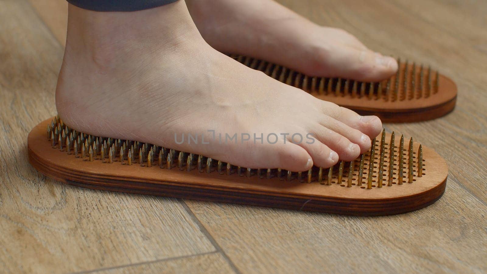 Female feet standing on boards with nails, close up. Media. Barefoot female standing on yoga nails board. by Mediawhalestock