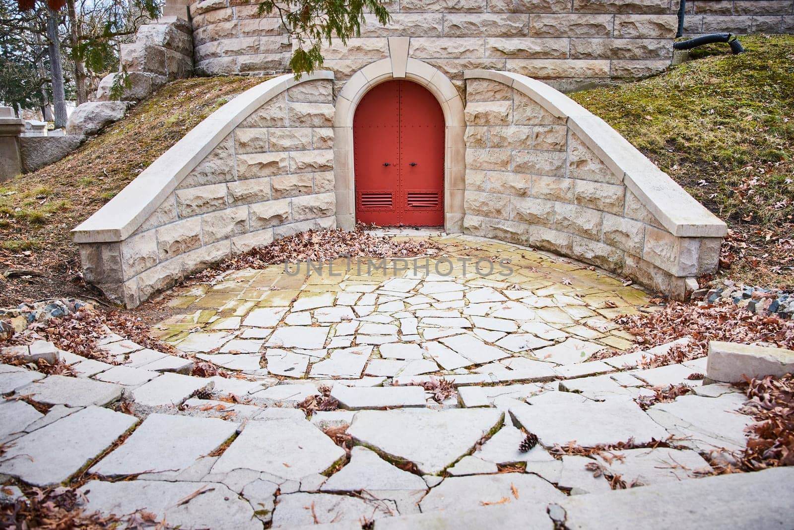 Enchanting red door in stone structure at Lindenwood Cemetery, Indiana, exuding a sense of mystery and tranquility amidst autumnal setting.