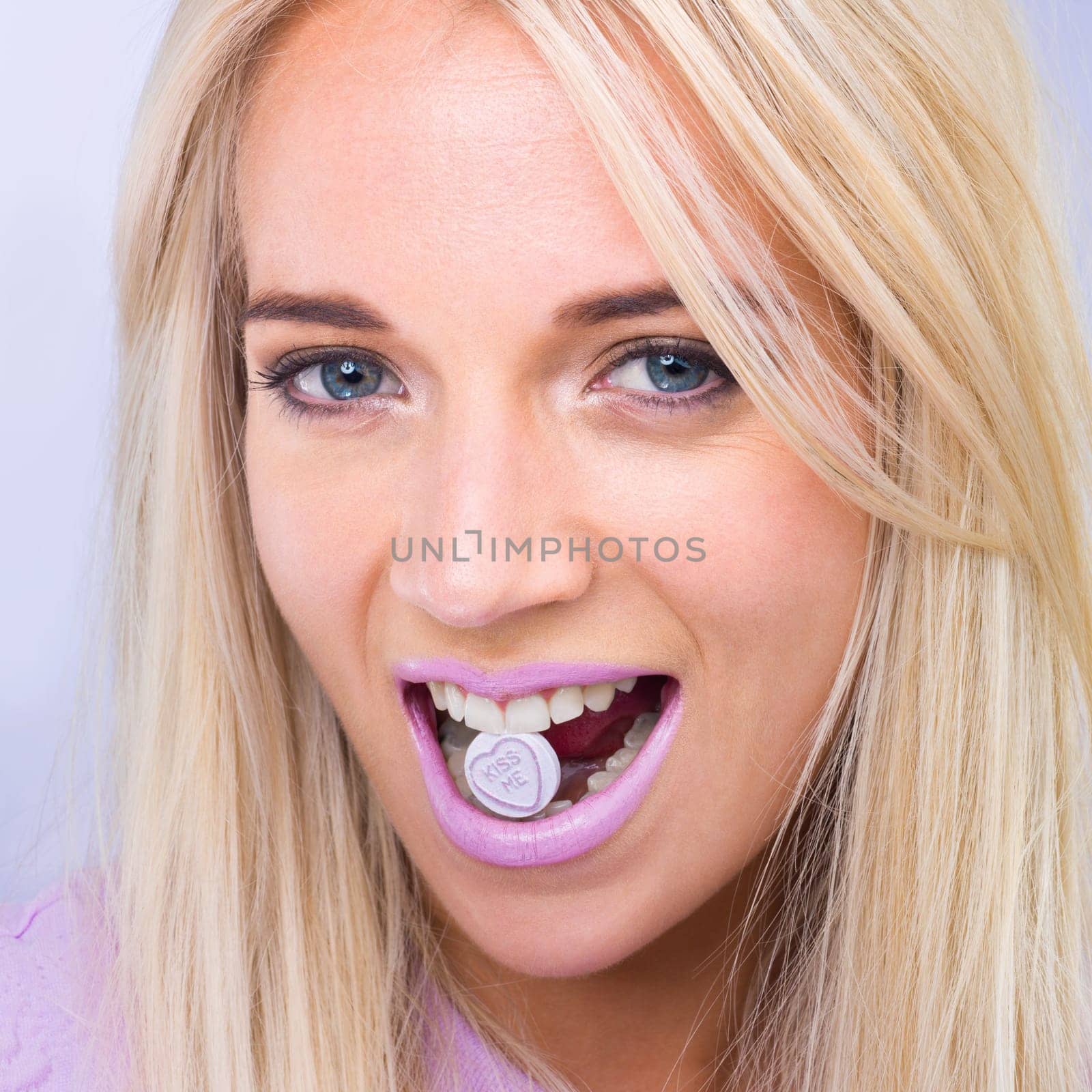 Woman, beauty and studio portrait with candy in mouth with makeup, lipstick or heart sign by purple background. Girl, person and model in closeup with sweets, emoji or happy for eating with cosmetics by YuriArcurs