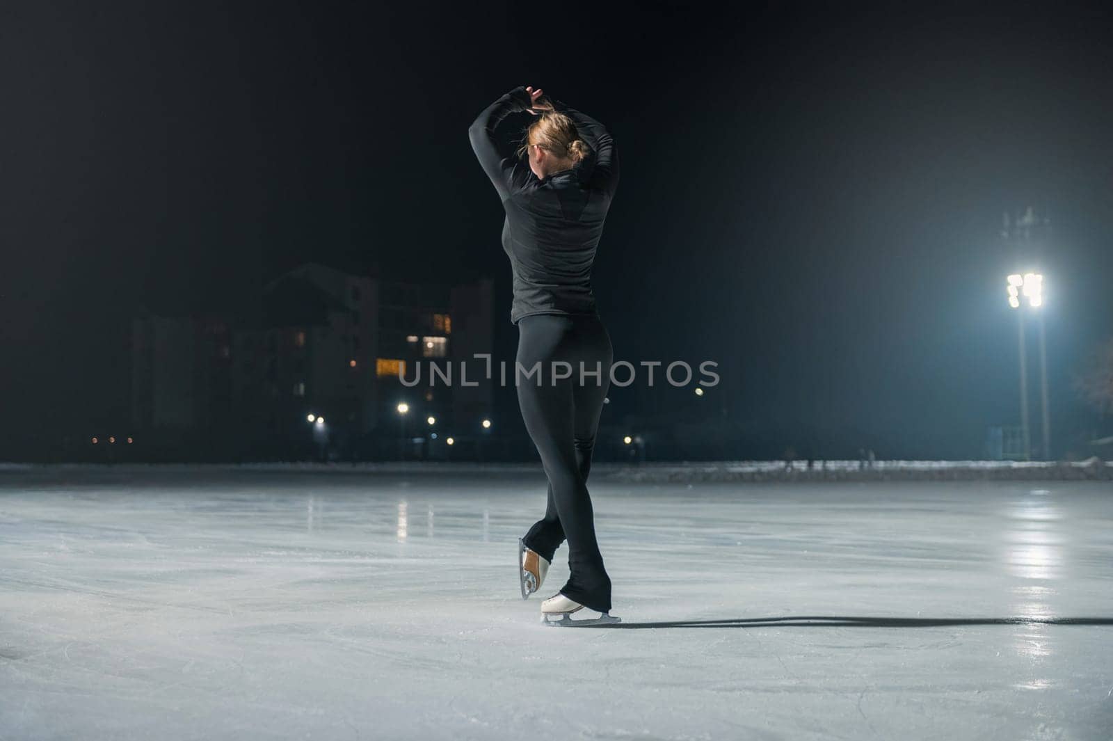 Beautiful young woman ice skating and performing she program over city outdoor ice arena. Winter activities concept