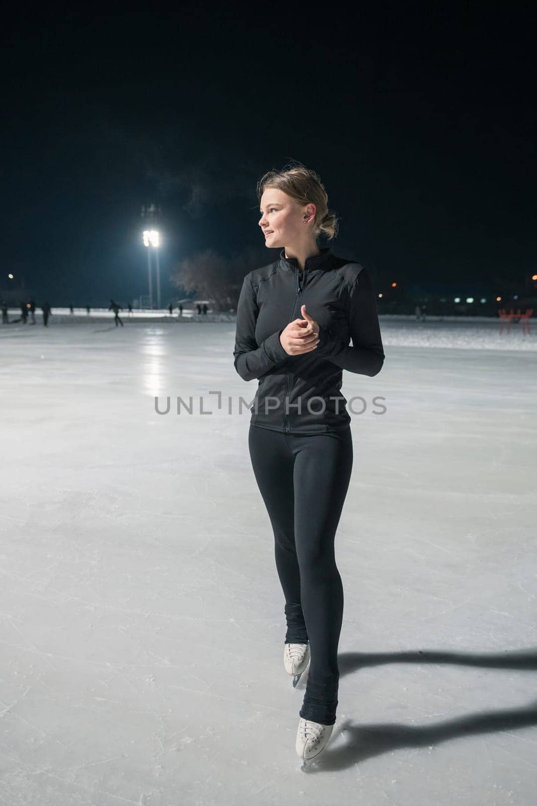 Beautiful young woman ice skating and performing she program over city outdoor ice arena. Winter activities concept