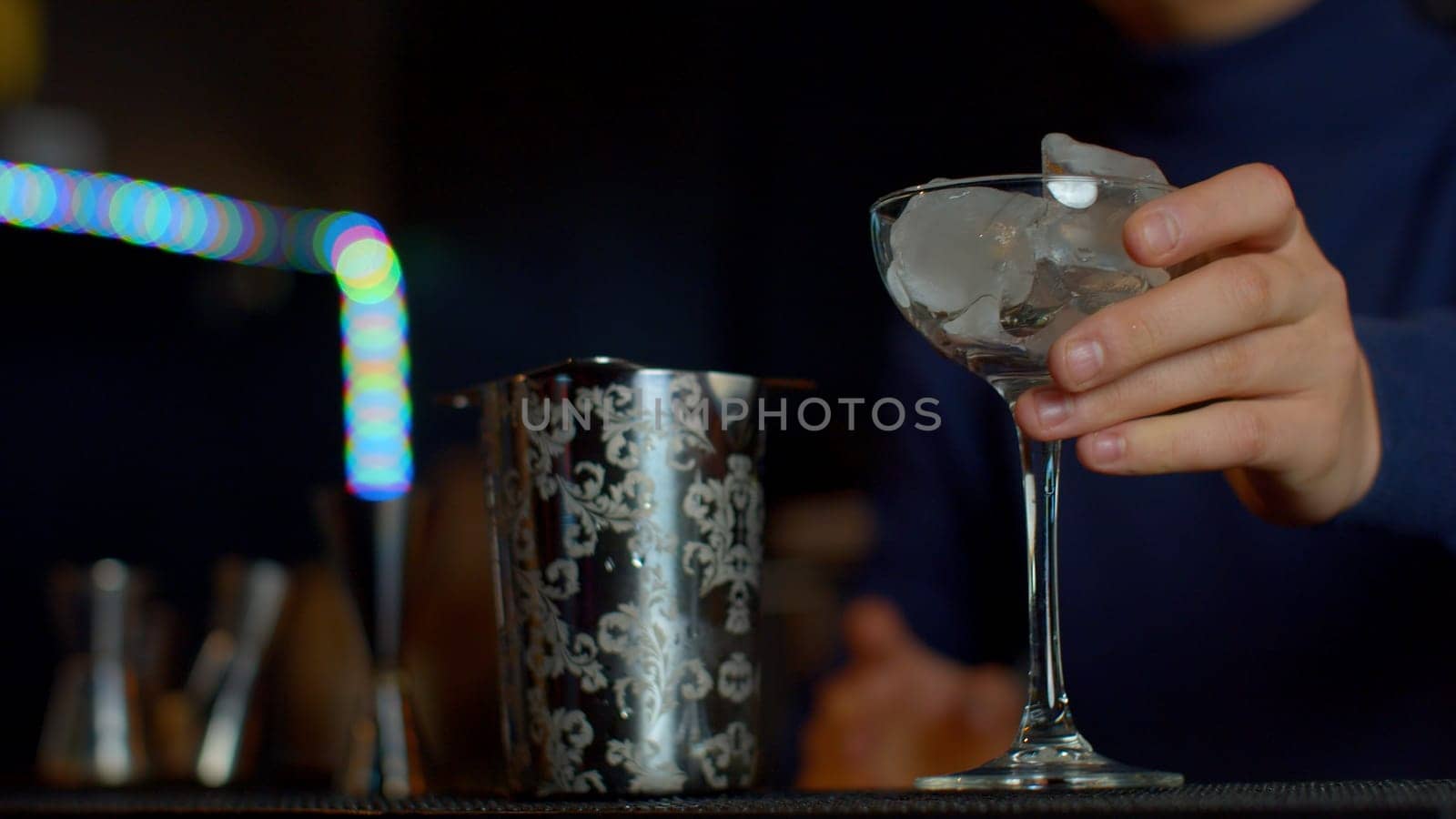 Close up bartender throwing away ice cubes from a small cocktail glass. Media. Cooling a glass for making a cocktail