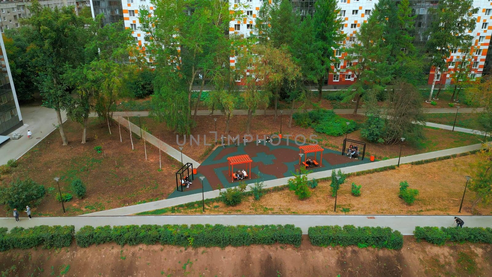 Top view of park alley in residential area of city. Clip. View of city with residential buildings and park alley. Beautiful landscape of park alley in urban landscape with buildings.