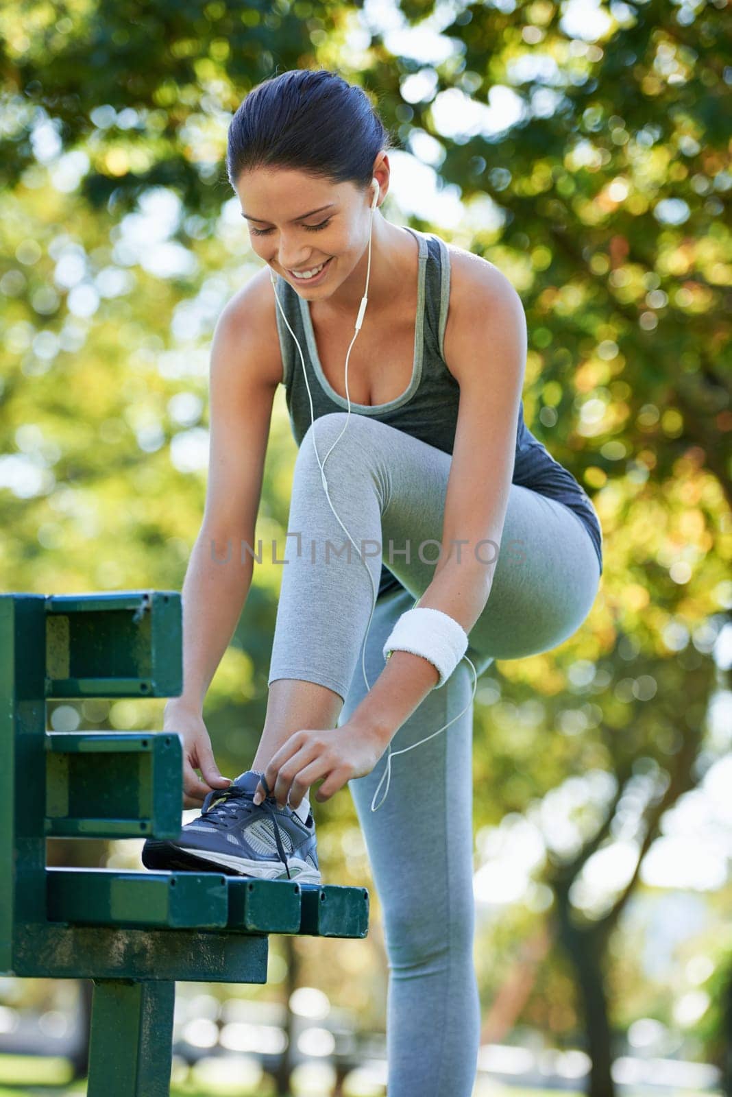 Happy woman, running or tying shoelaces in park, music or streaming audio for exercise in nature. Lady, smile or wellness with earphones for jog, fitness or training performance in outdoor in summer.