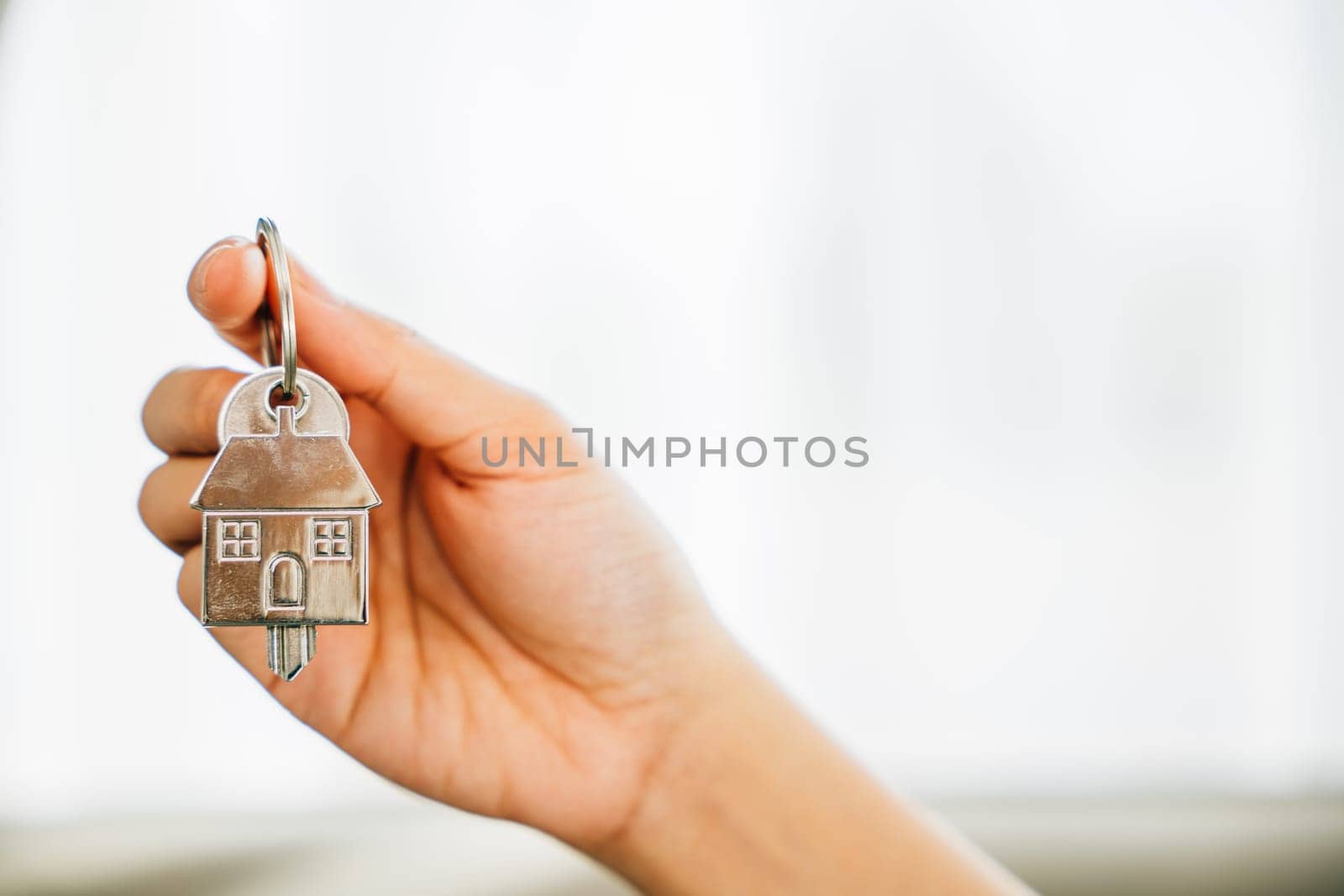 A woman's hand holds house key highlighting homeowners' achievement by Sorapop