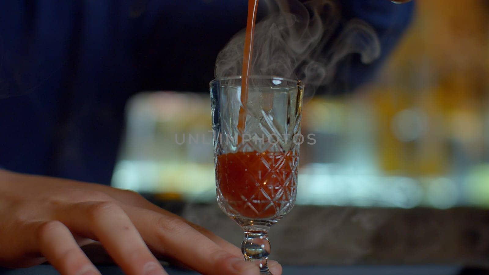 Close up of bartender at a bar counter pouring alcohol into vintage glass. Media. Pouring red hot alcoholic tincture with steam