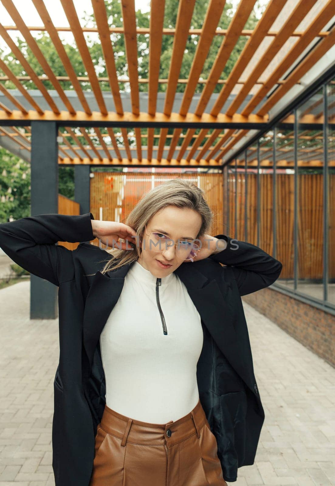 A woman wearing a white top and brown pants standing casually outdoors.