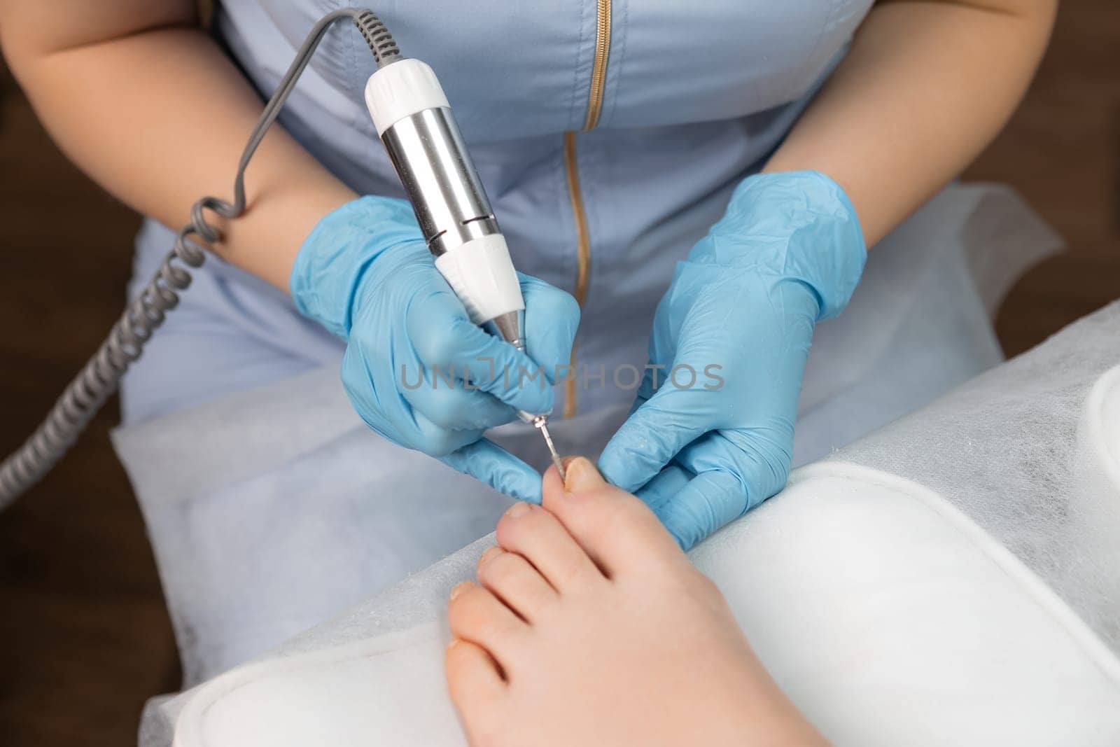Young woman getting professional pedicure with milling cutter in beauty salon.